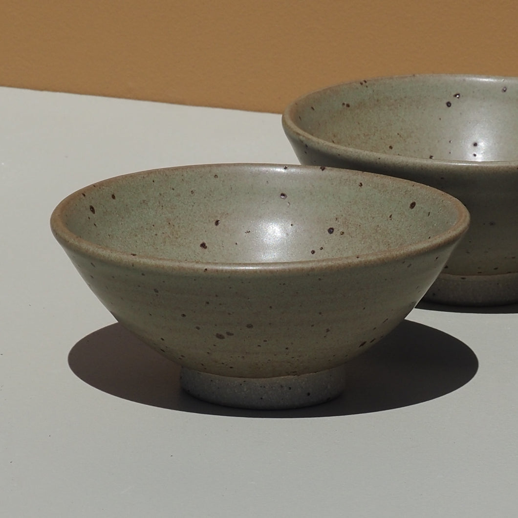 Two ceramic bowls with speckled glaze on a plain background