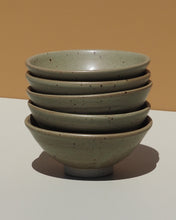 Stack of five sage green ceramic bowls with a speckled pattern on a neutral background