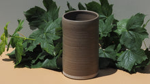 Brown ceramic vase with green leaves on a beige surface